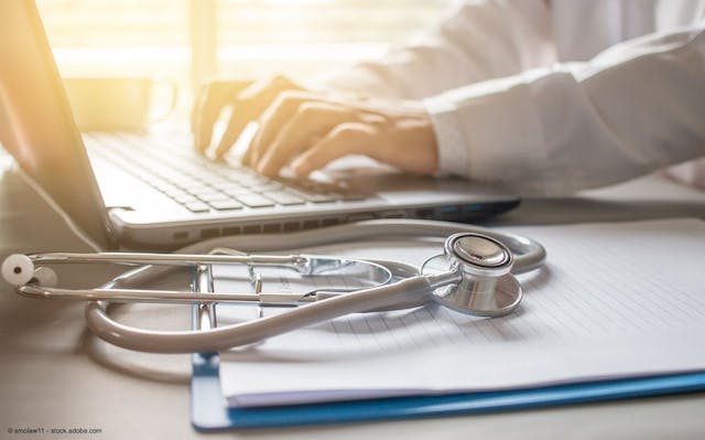 stethoscope in foreground, doctor typing on laptop blurred in background